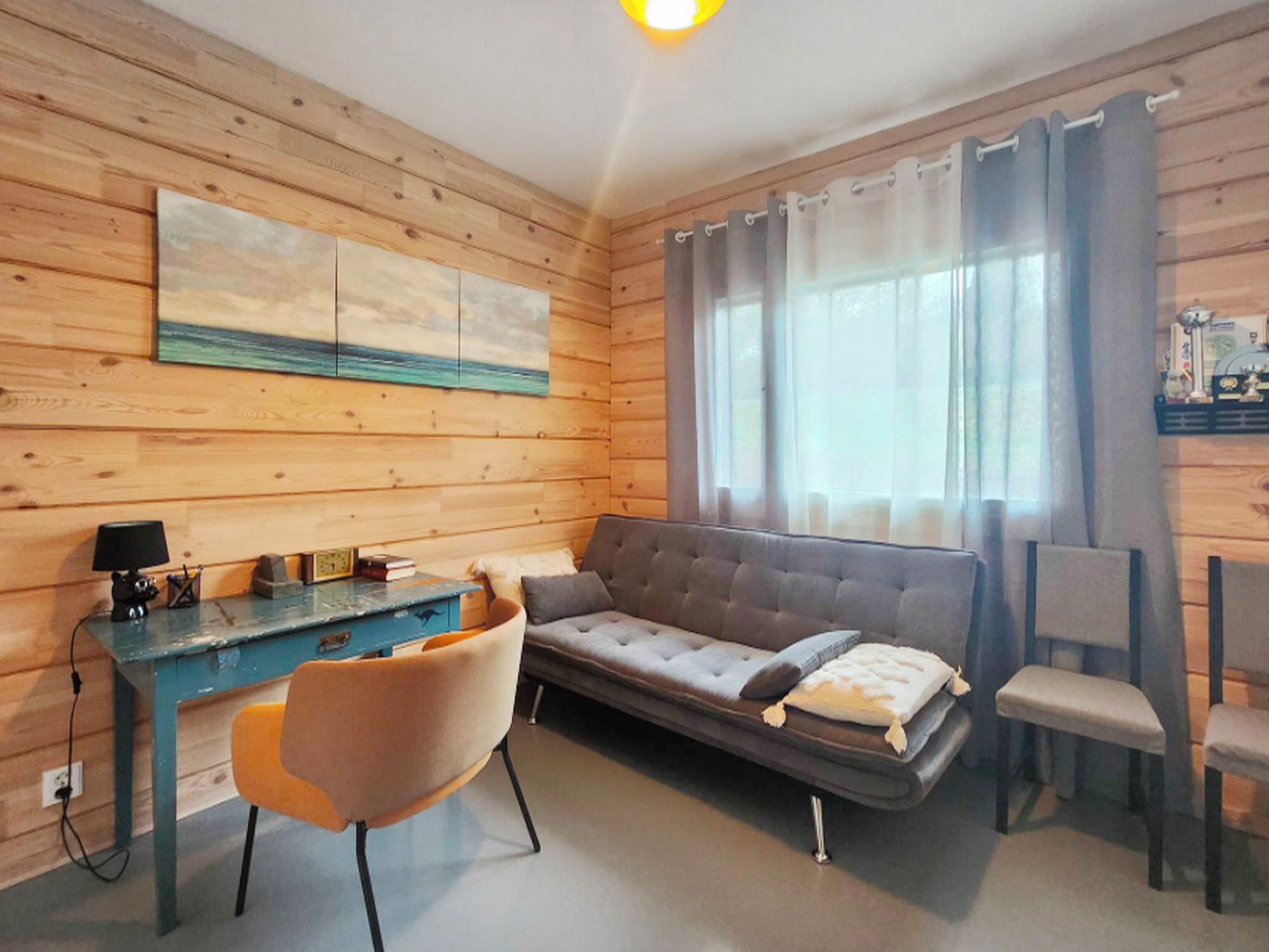 Une pièce chaleureuse avec un décor intérieur en bois, un canapé, un bureau avec une lampe et une fenêtre avec des rideaux.