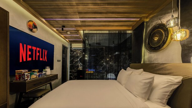 Une chambre d’hôtel avec un grand lit, un téléviseur affichant le logo de Netflix, une horloge murale et un élément décoratif mural.