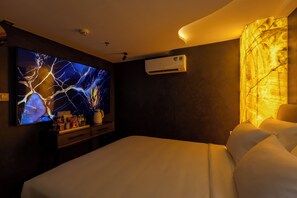 A hotel room with a large flat-screen TV, a minibar, an air conditioning unit, and a bed with white bedding. - Pynt Hotel 4 (Ho Chi Minh City)