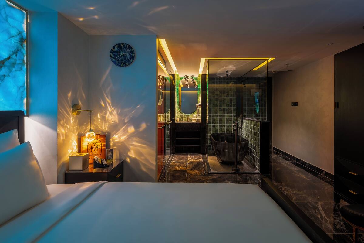 A modern hotel room with a bed, bedside table, lamp, and a view of the bathroom.