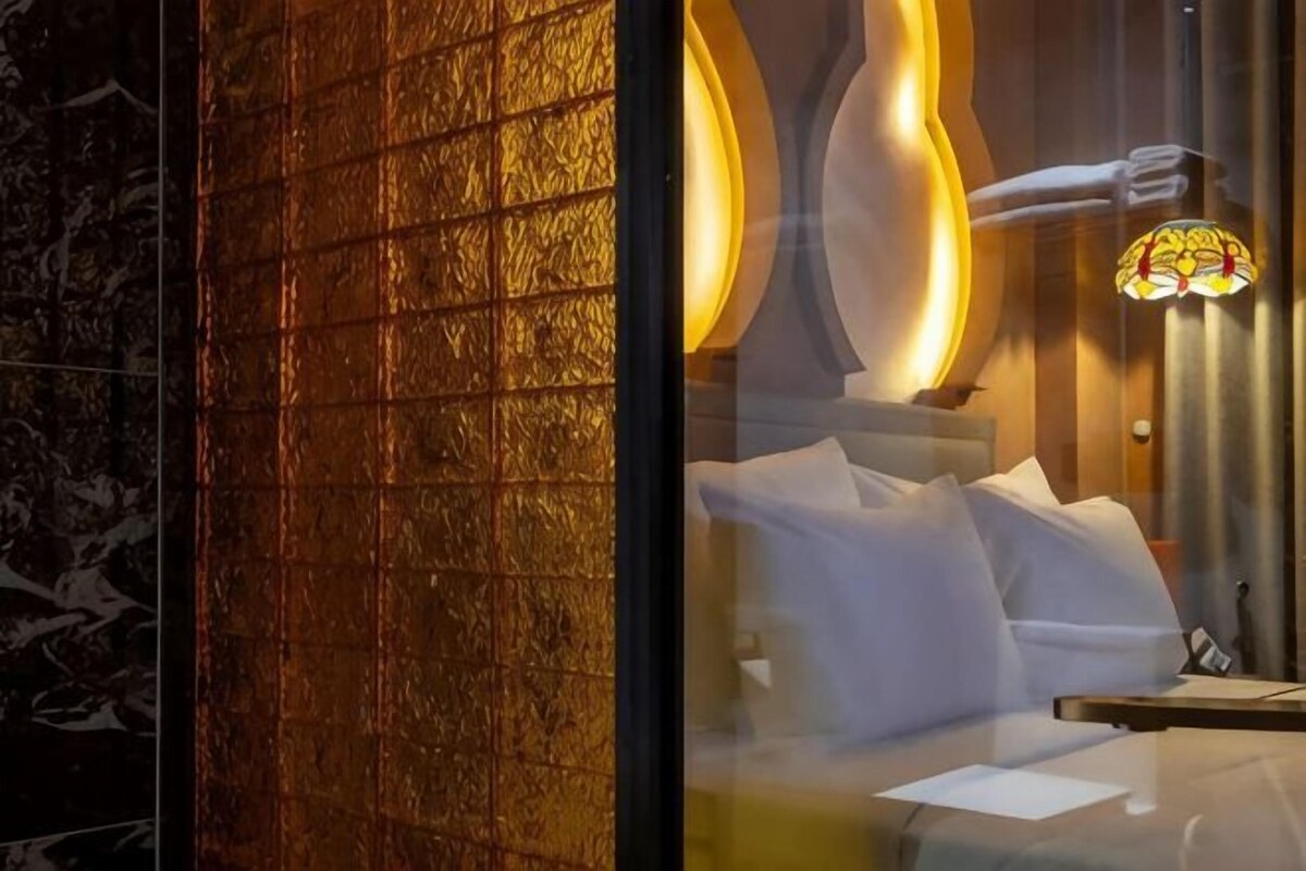 Une chambre d’hôtel avec un lit, une grande fenêtre et un mur orné d’un motif texturé.