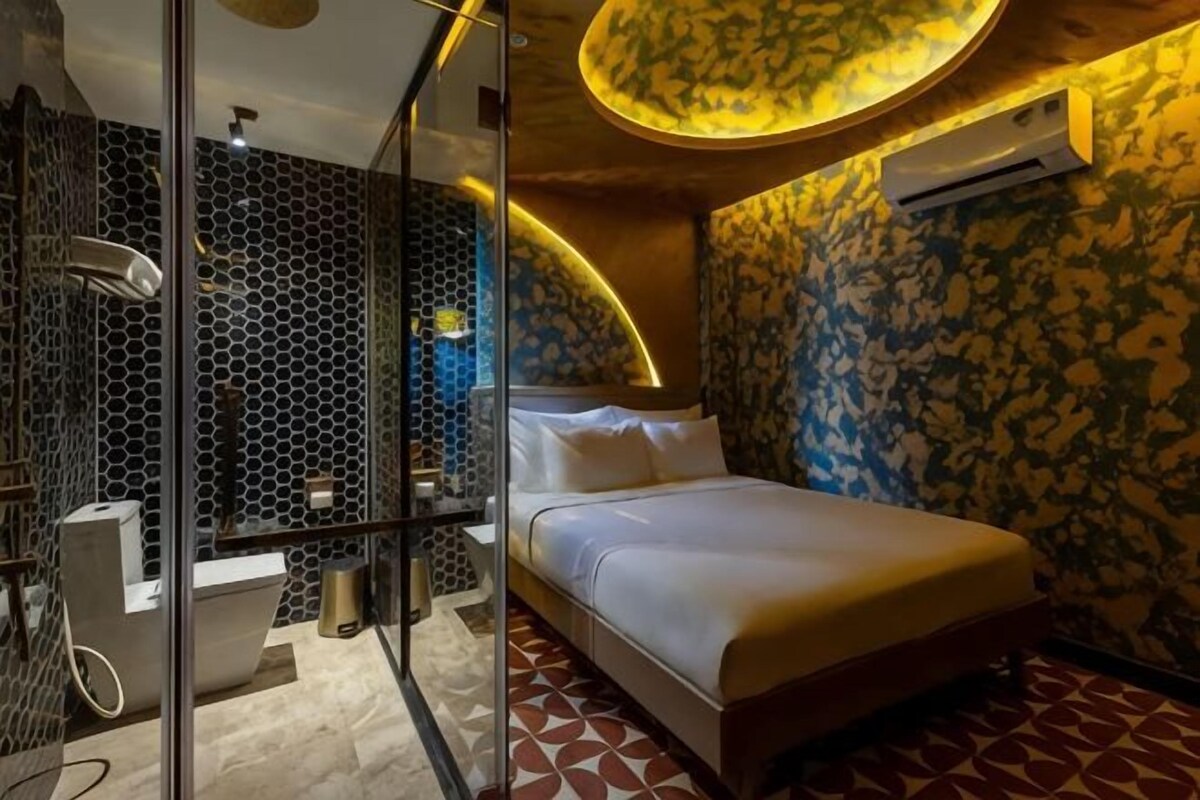 Une chambre moderne dotée d’une douche à parois de verre, d’un lit avec une literie blanche et d’un motif mural original.