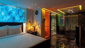 Une chambre d’hôtel moderne équipée d’un lit, d’une table de chevet, d’une horloge murale et d’une salle de bain avec une cabine de douche en verre.