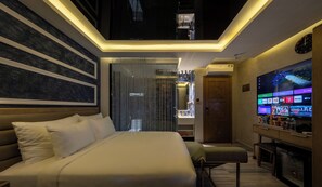 Een moderne hotelkamer met een groot bed, een tv waarop verschillende zenders worden getoond, en een plafond met ingebouwde verlichting.