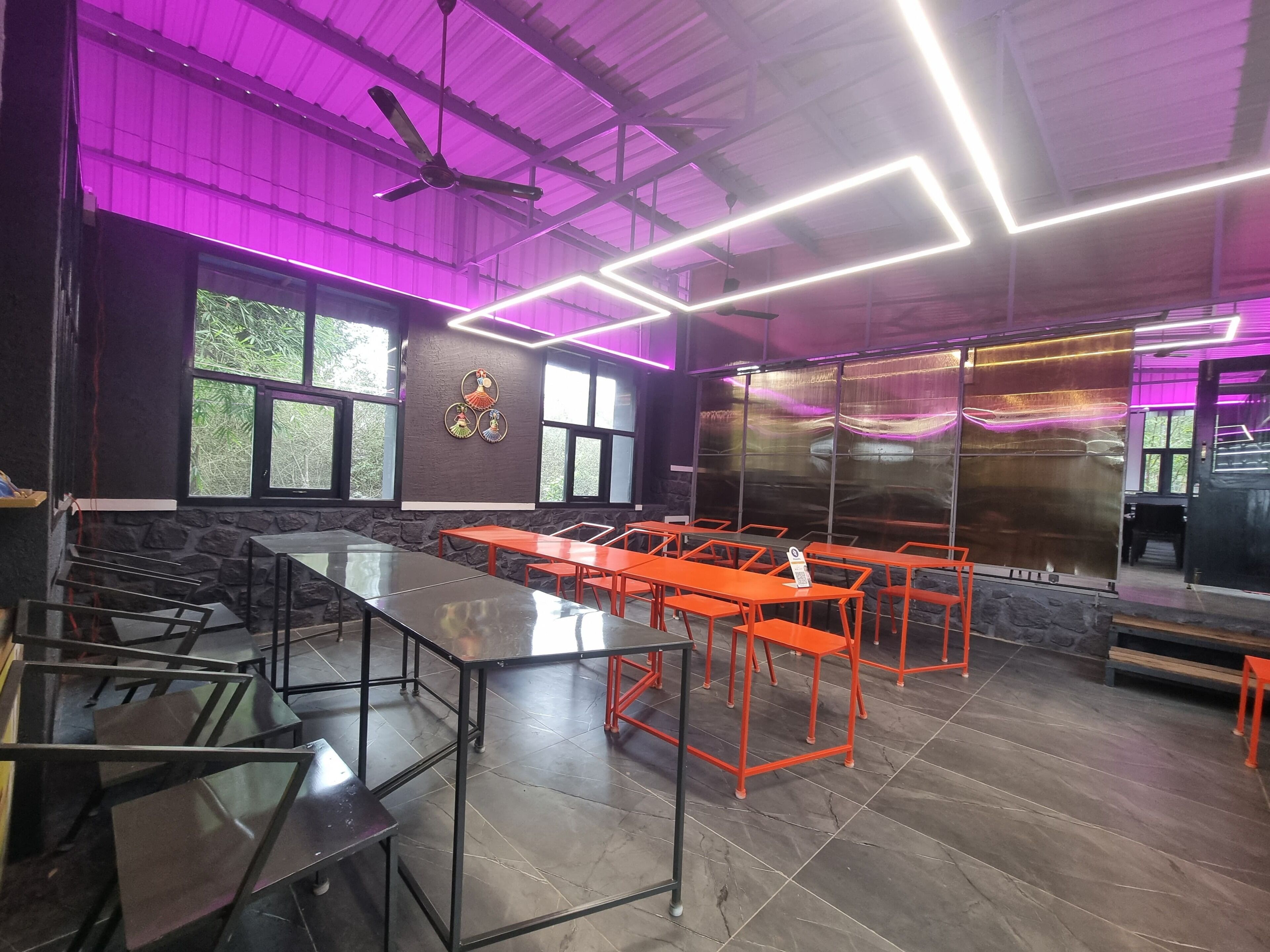 A restaurant interior with a mix of black and orange tables, a stone wall, and large windows.