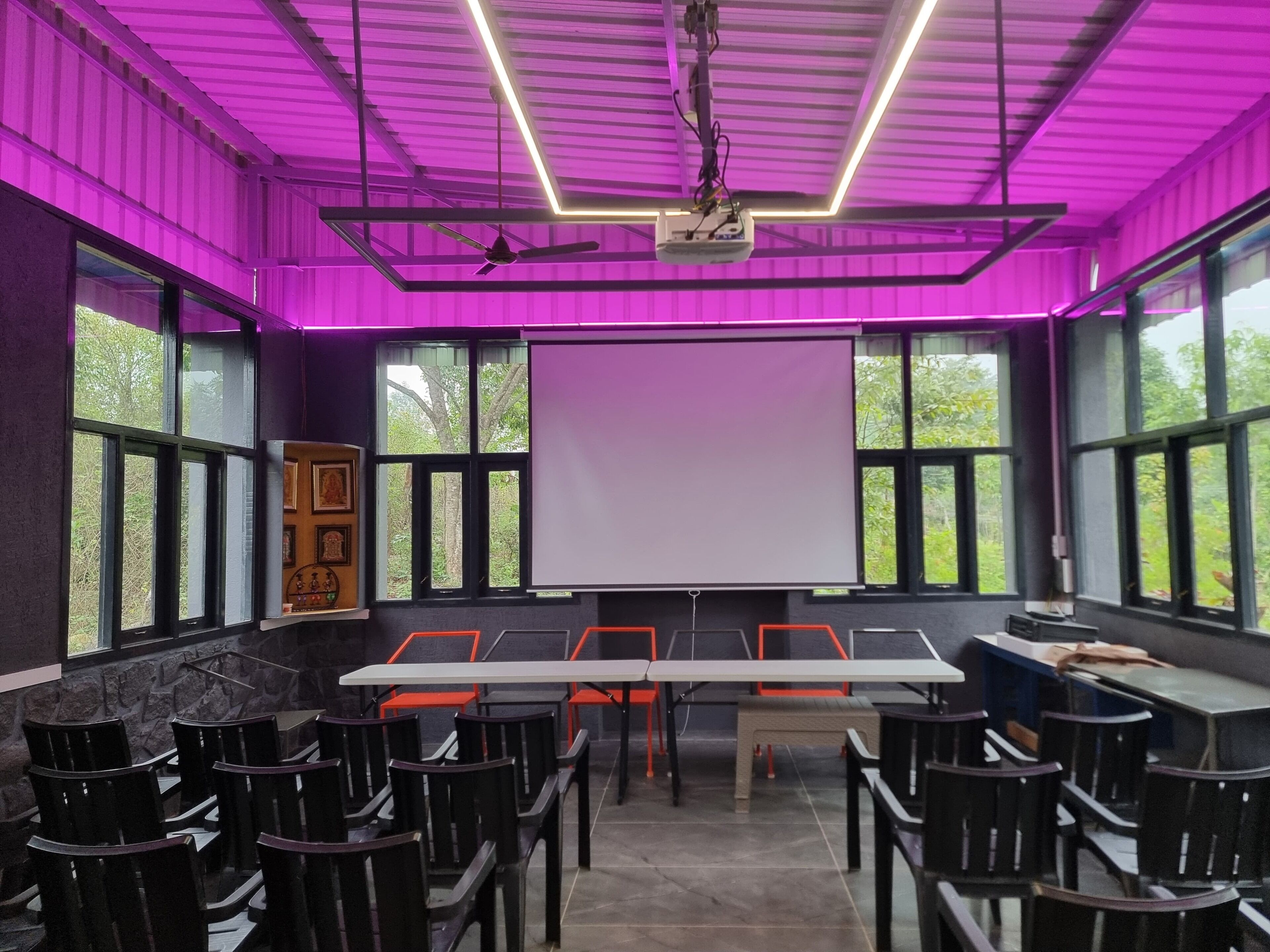 Un salón de conferencias con una gran mesa, sillas, una pantalla de proyector y ventanas con vistas a zonas verdes.