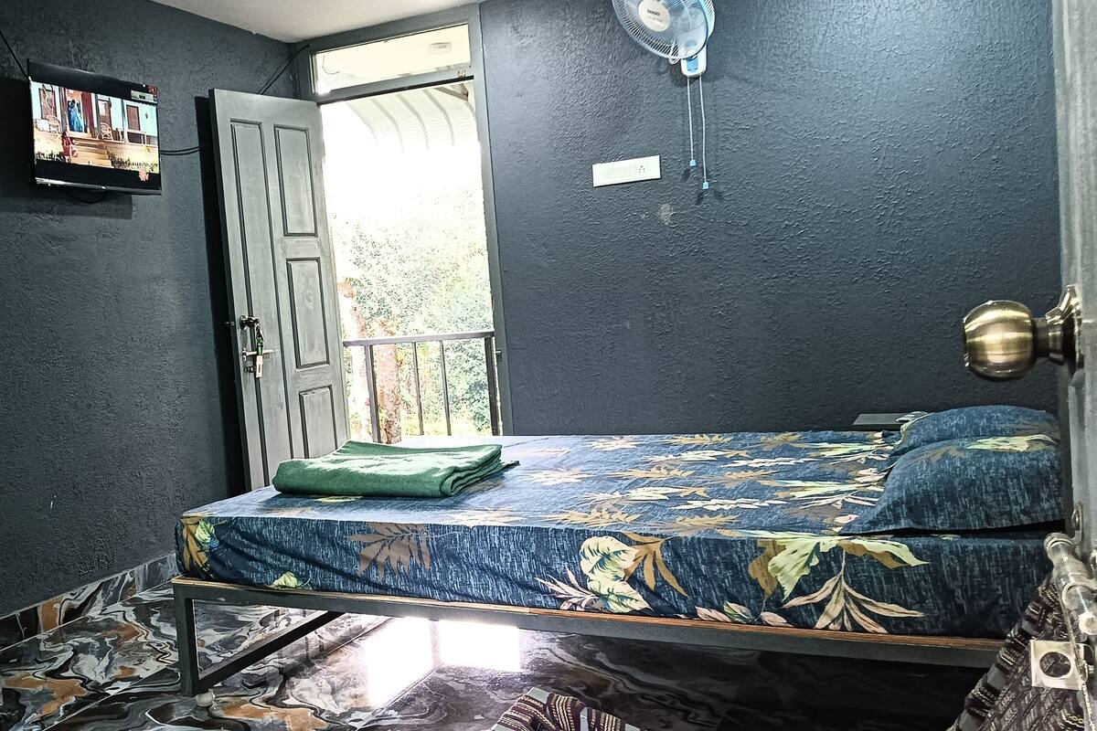Habitació amb un llit, una televisió penjada a la paret i una porta que dona a una zona exterior.