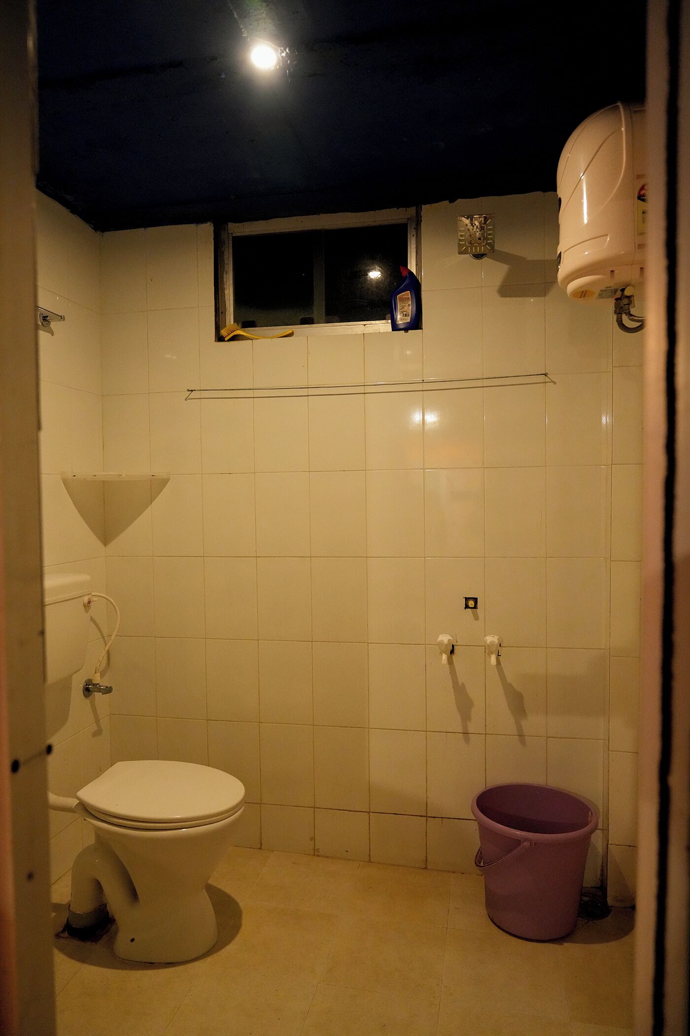 A small bathroom with a toilet, a window, and a bucket.