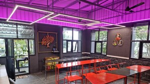 A modern indoor space with a high ceiling, large windows, and red tables and chairs. - BlueHill Lotus Holistic Wellness Village (Sirumalai)