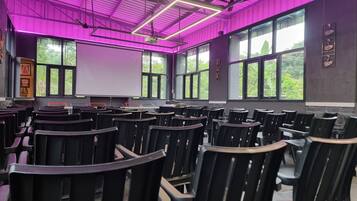 A classroom with rows of black chairs, a projector screen, and large windows.