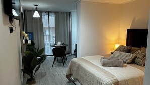 Una habitación de hotel con cama, mesita de noche, lámpara y televisor montado en la pared.