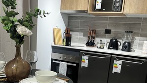 Una cocina moderna con armarios de madera, un microondas, un hervidor y una licuadora sobre la encimera. Hay una mesa de comedor con un jarrón de flores, platos y un tazón.
