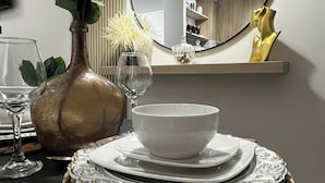 Una mesa de comedor con un cuenco blanco, un vaso y un florero con flores. Un espejo refleja la habitación.