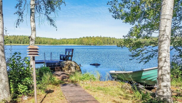 Un sentier en bois mène à un quai au bord d’un lac, avec une chaise et un bateau à proximité.
