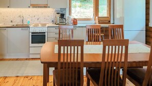 Une cuisine compacte avec des meubles blancs, une cuisinière, un four et un réfrigérateur. On y trouve une table à manger avec quatre chaises en bois.