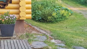 Une cabane en rondins dotée d’une terrasse en bois et d’un chemin de pierre menant à un jardin luxuriant.