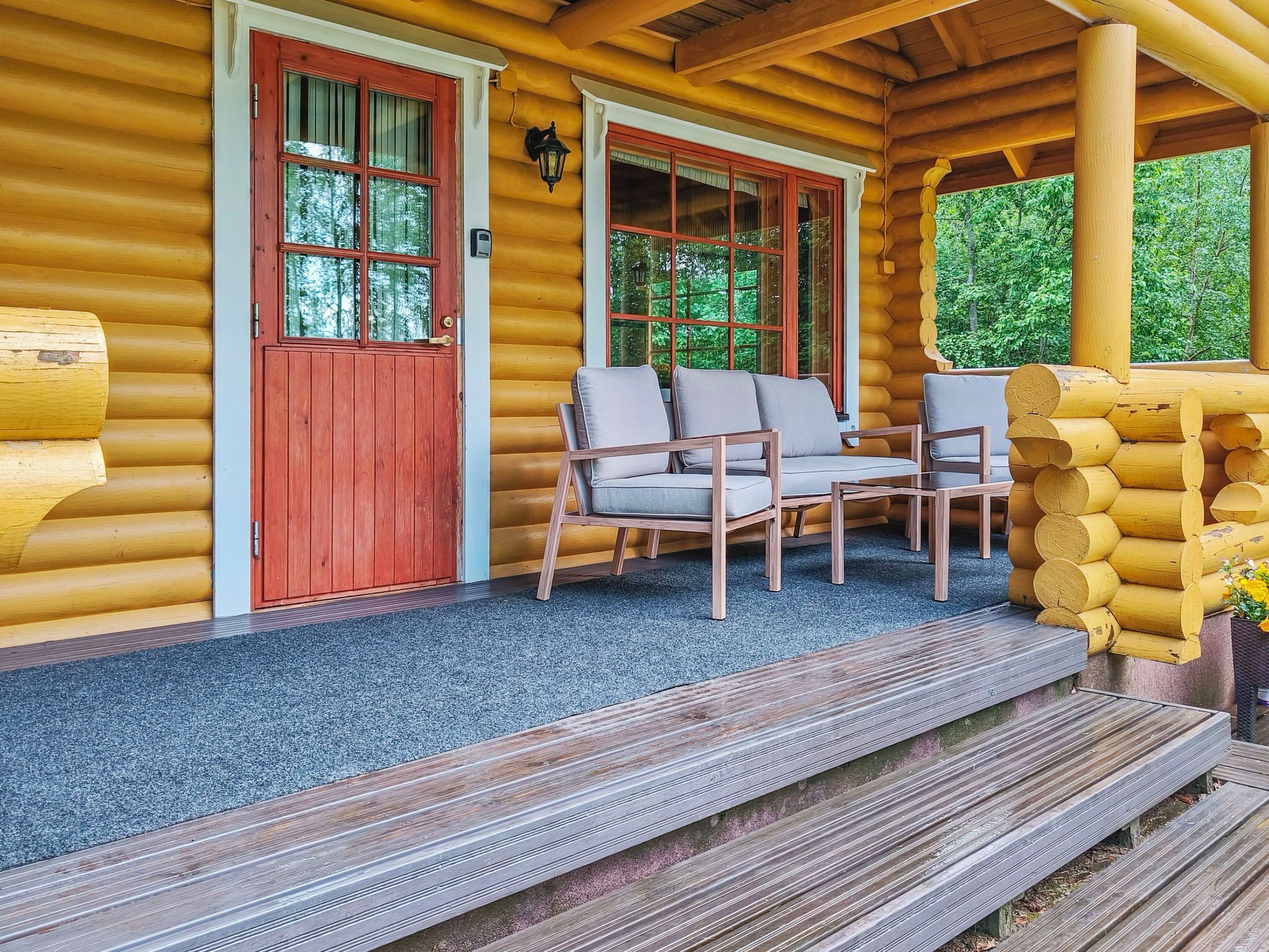 A log cabin with a porch, two wooden chairs, and a red door.