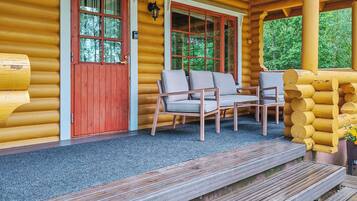 A log cabin with a porch, two wooden chairs, and a red door.