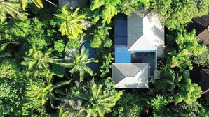 An aerial view of a house surrounded by dense tropical vegetation, including palm trees and various shrubs. - The Ubāri Bali (Ubud)