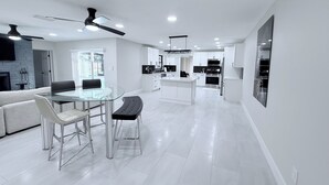 A modern kitchen with white cabinetry, a central island, and a dining area with a glass table and chairs. - This is it: Red Door Vacay House in Delightful Brandon with Game Room and Pool (Brandon)