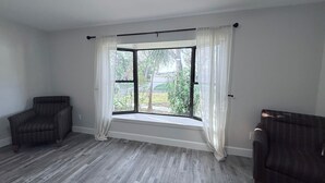 A room with a large window, two armchairs, and a wooden floor. - This is it: Red Door Vacay House in Delightful Brandon with Game Room and Pool (Brandon)