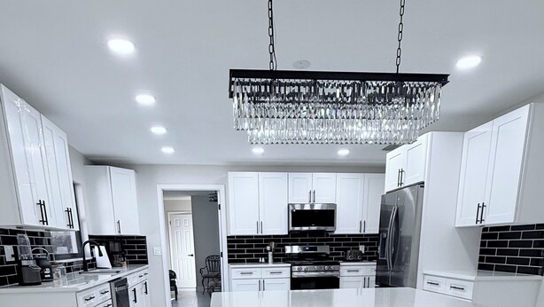 A modern kitchen with white cabinetry, a central island, stainless steel appliances, and a decorative chandelier. - This is it: Red Door Vacay House in Delightful Brandon with Game Room and Pool (Brandon)