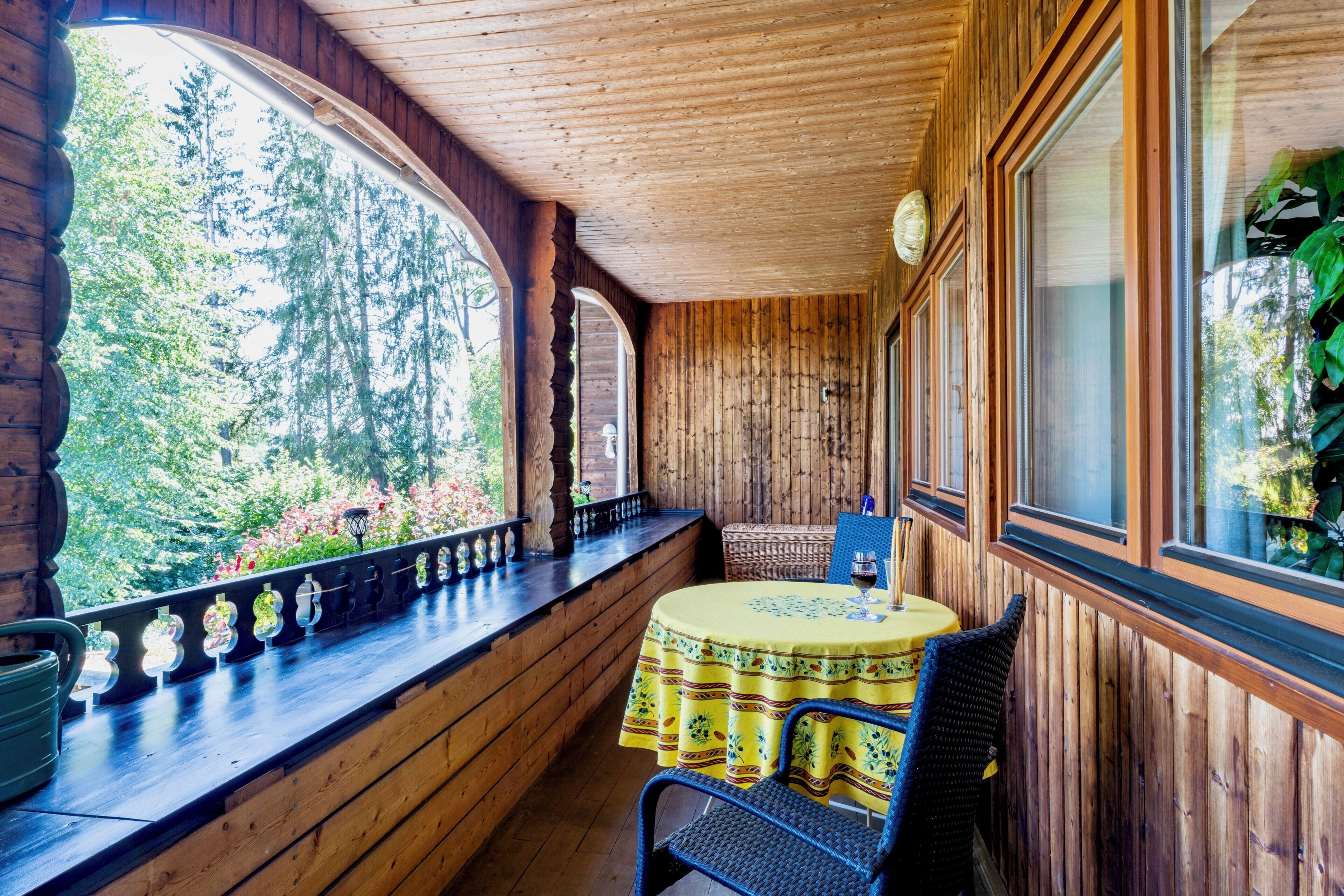 A wooden cabin with a balcony, a table with a yellow tablecloth, and a chair.
