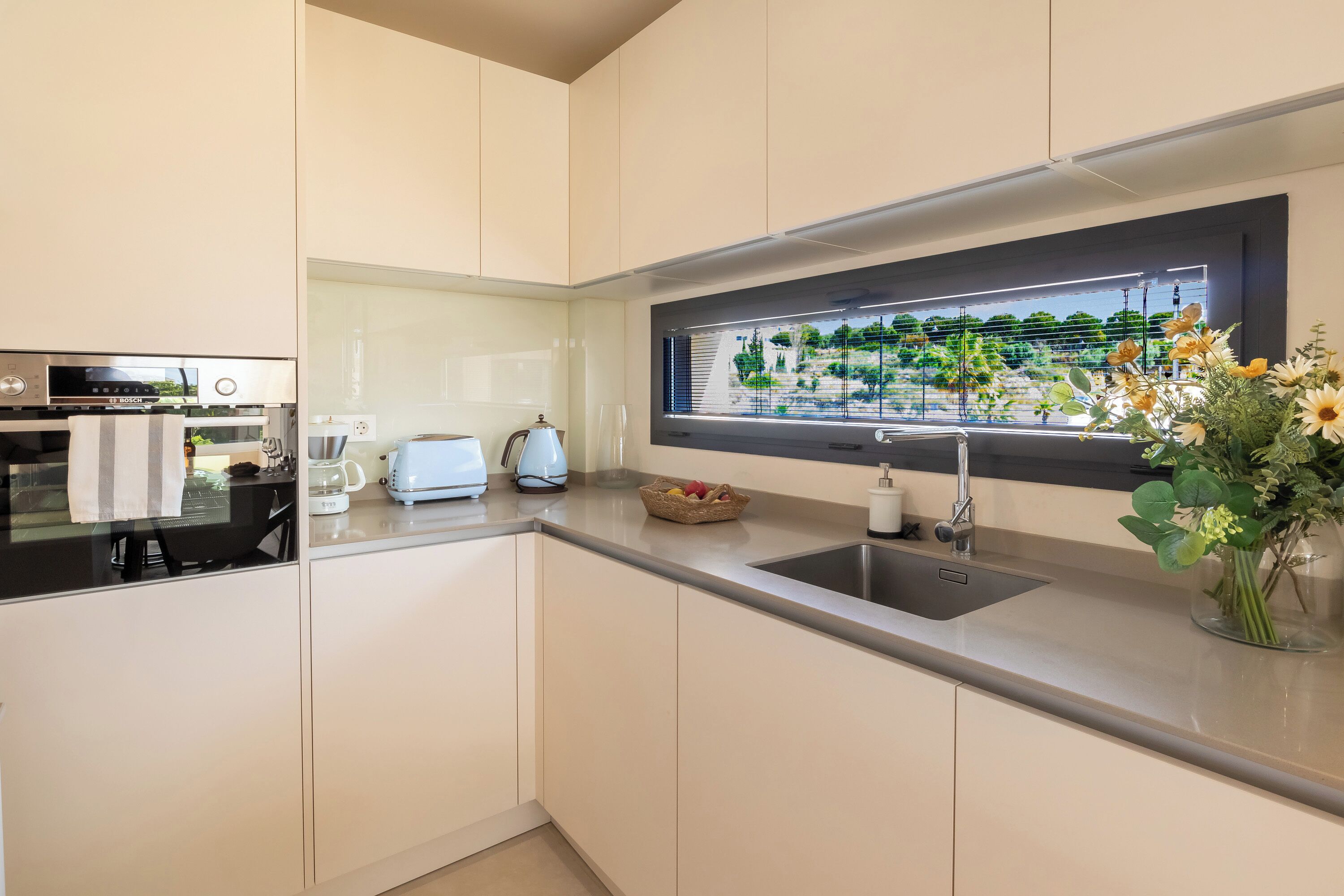 Una cocina moderna con horno integrado, cafetera y ventana con vista a la vegetación.