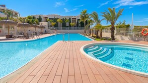 Ein Swimmingpool mit Liegestühlen und Sonnenschirmen, umgeben von Palmen und blauem Himmel.