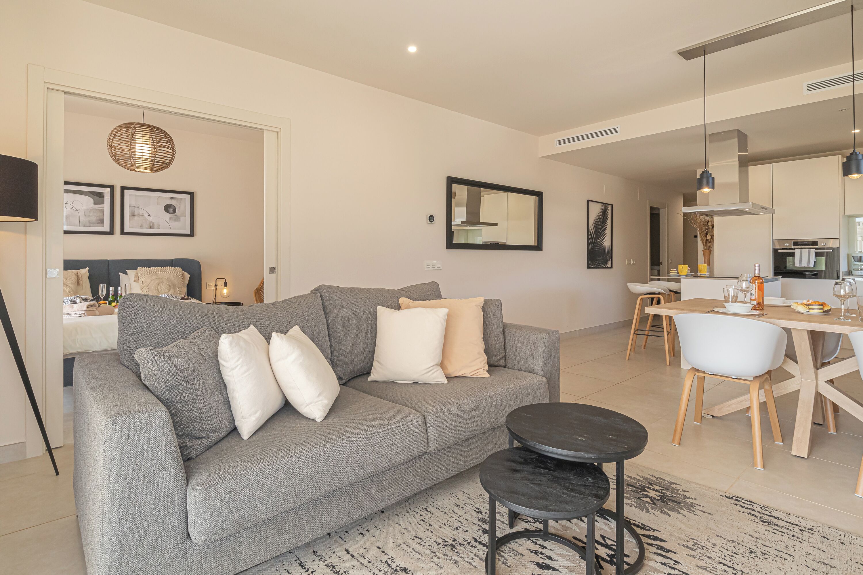 A modern living room with a grey sofa, a coffee table, and a dining area with a table and chairs.