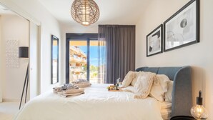 Ein modernes Schlafzimmer mit einem großen Bett, einem Nachttisch mit Lampe und Blick ins Freie.