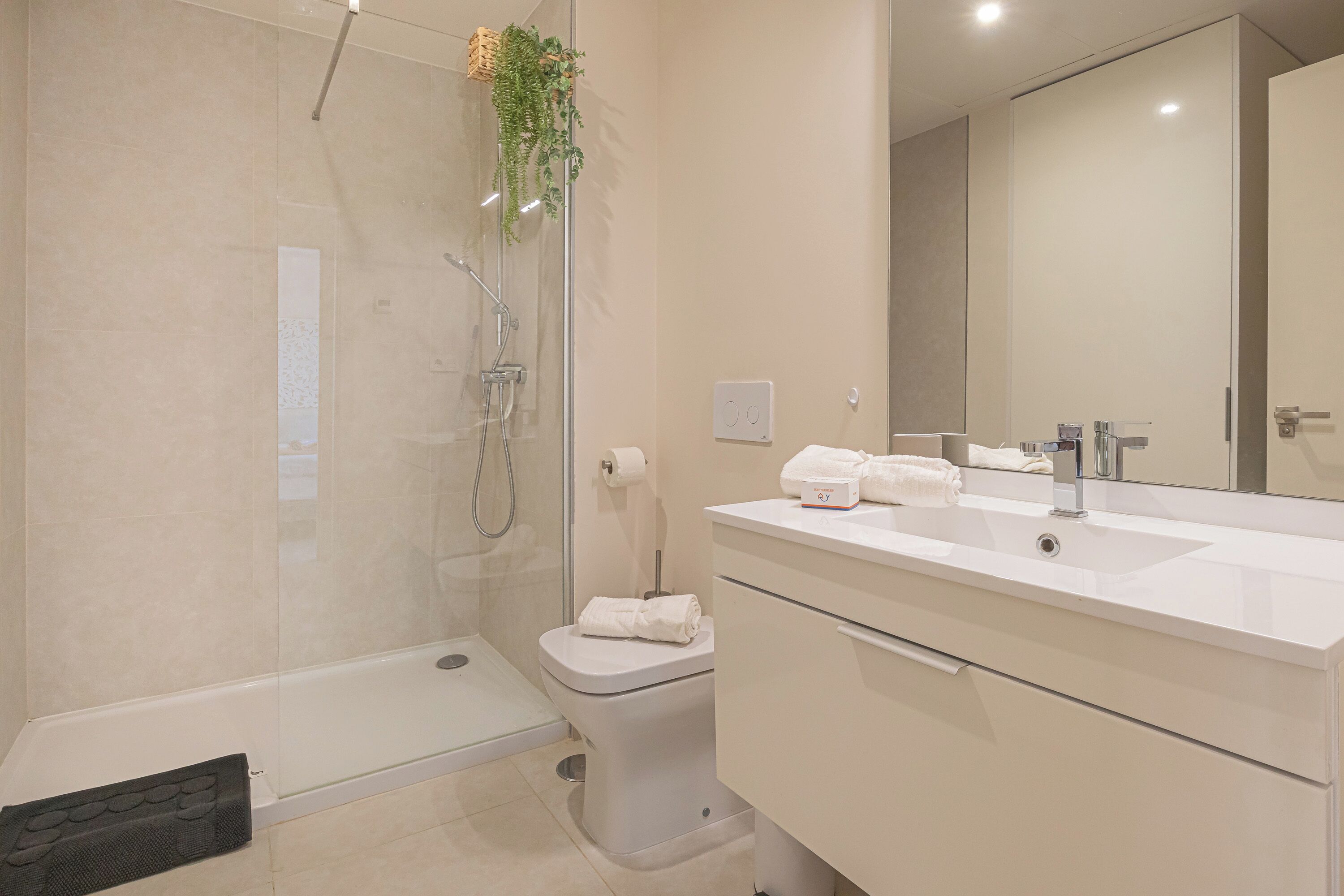 Un bagno moderno con doccia vetro, water, lavandino con specchio e portasciugamani.