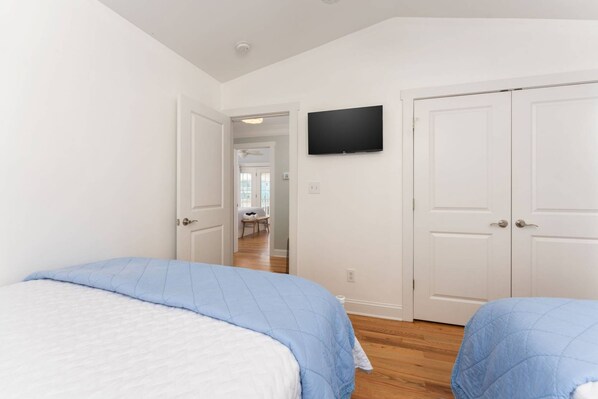 Une chambre avec deux lits, un téléviseur fixé au mur et une porte donnant sur une autre pièce.