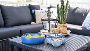 Un espace patio avec une table en osier, des bols rayés de bleu et de blanc, une plante en pot et une lanterne.