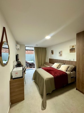 Une chambre dâhĂŽtel avec un lit, un petit bureau dotĂ© dâun micro-ondes, une chaise, une fenĂȘtre avec des rideaux et une vue sur un immeuble en briques.