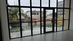 A room with large windows, a tiled floor, and a view of residential buildings and a car outside.