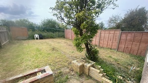 Un jardin avec un petit arbre, un mur de briques et une clôture en bois.