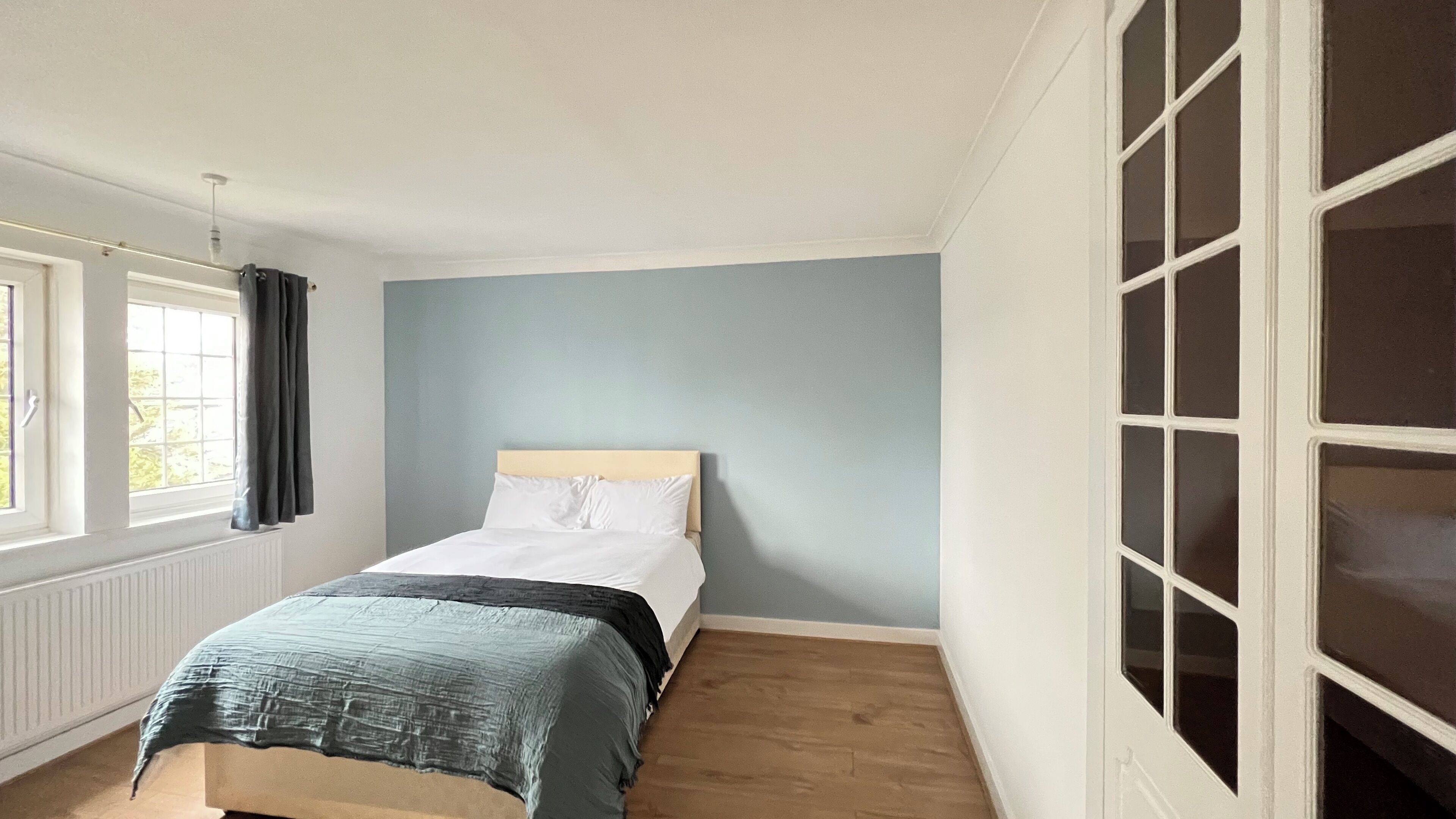 A bedroom with a bed, a window, and a door with glass panels.