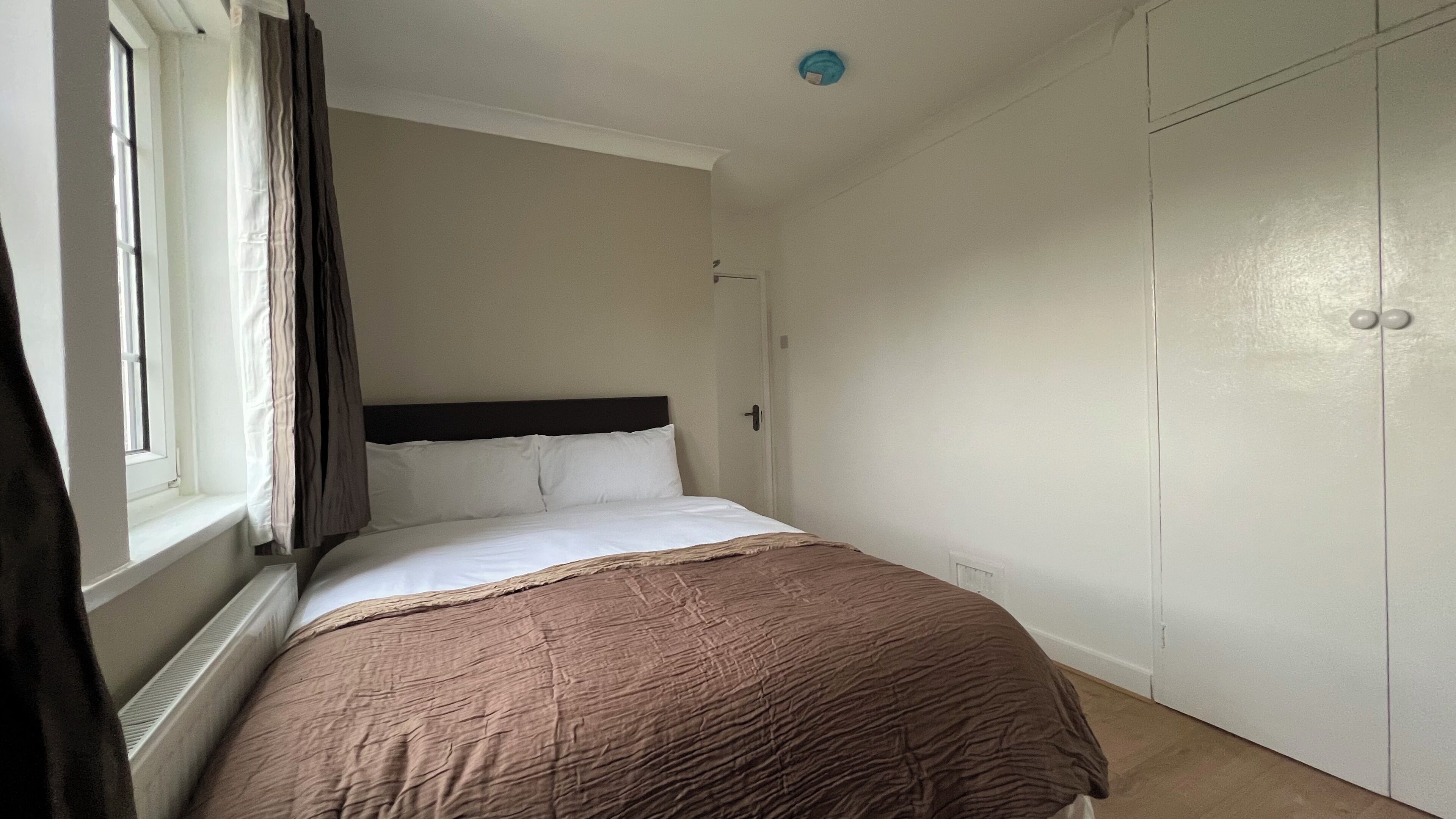 A bedroom with a bed, a window with curtains, a wardrobe, and a door.