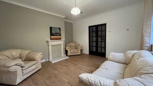 Un salon doté d’une cheminée, de deux fauteuils en cuir, d’un canapé blanc et d’une porte dont les panneaux sont en verre dépoli.