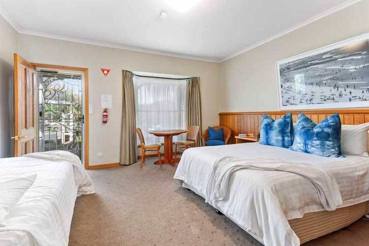 Ein Hotelzimmer mit zwei Betten, einem Esstisch und einem großen Fenster mit Vorhängen.