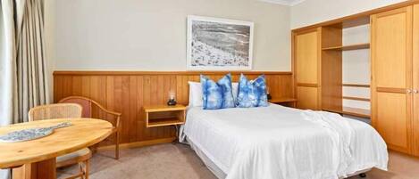 Una habitación de hotel con una cama, una mesita de noche de madera, una silla, una mesa y un armario.