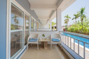 A balcony with two wicker chairs, a small table with a vase, and a poolside view. - Alaya Stays Gracias Seaora Retreat (Morjim)