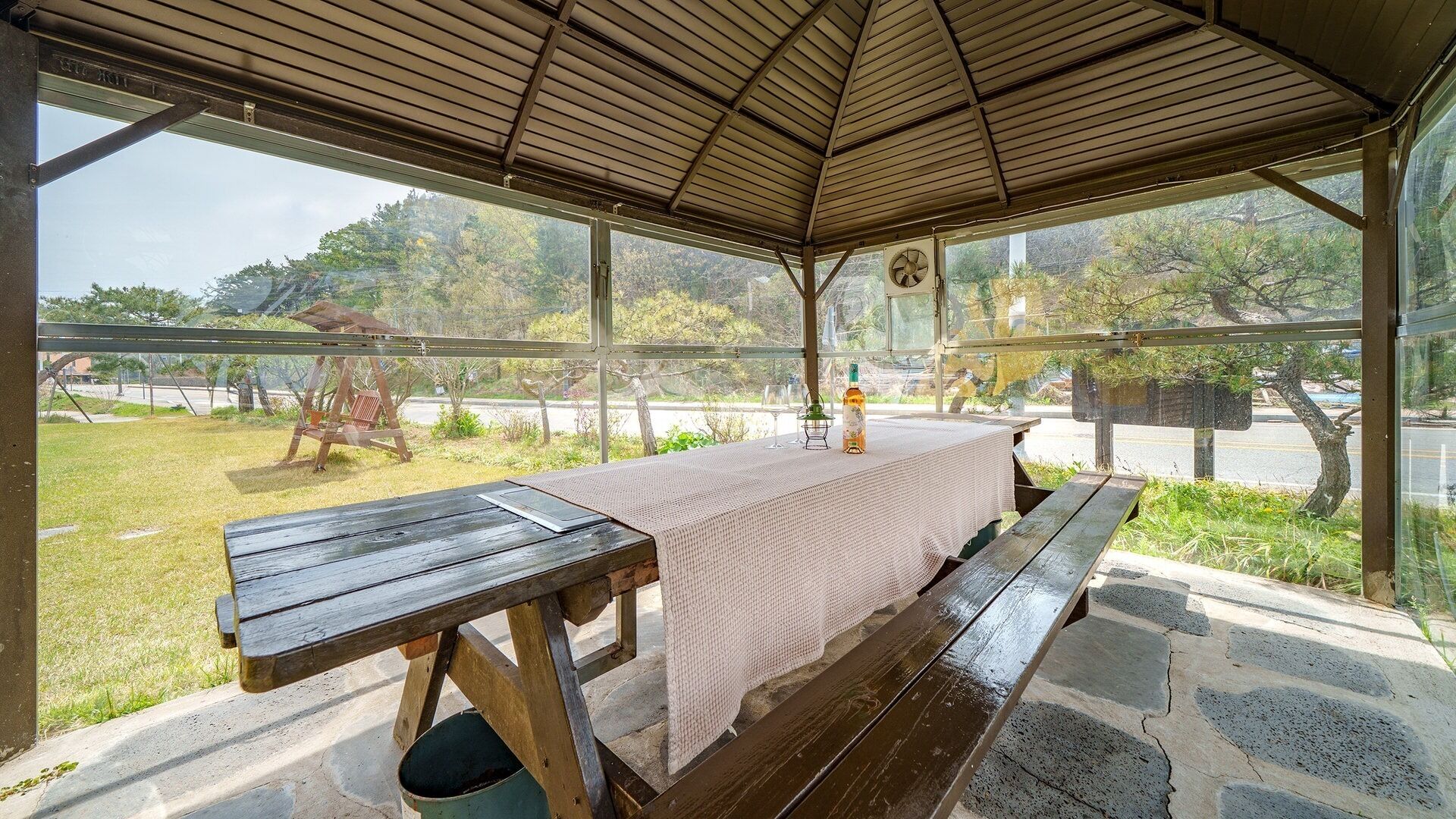 Un espace extérieur abrité avec une table de pique-nique, un banc et une bouteille d’alcool.