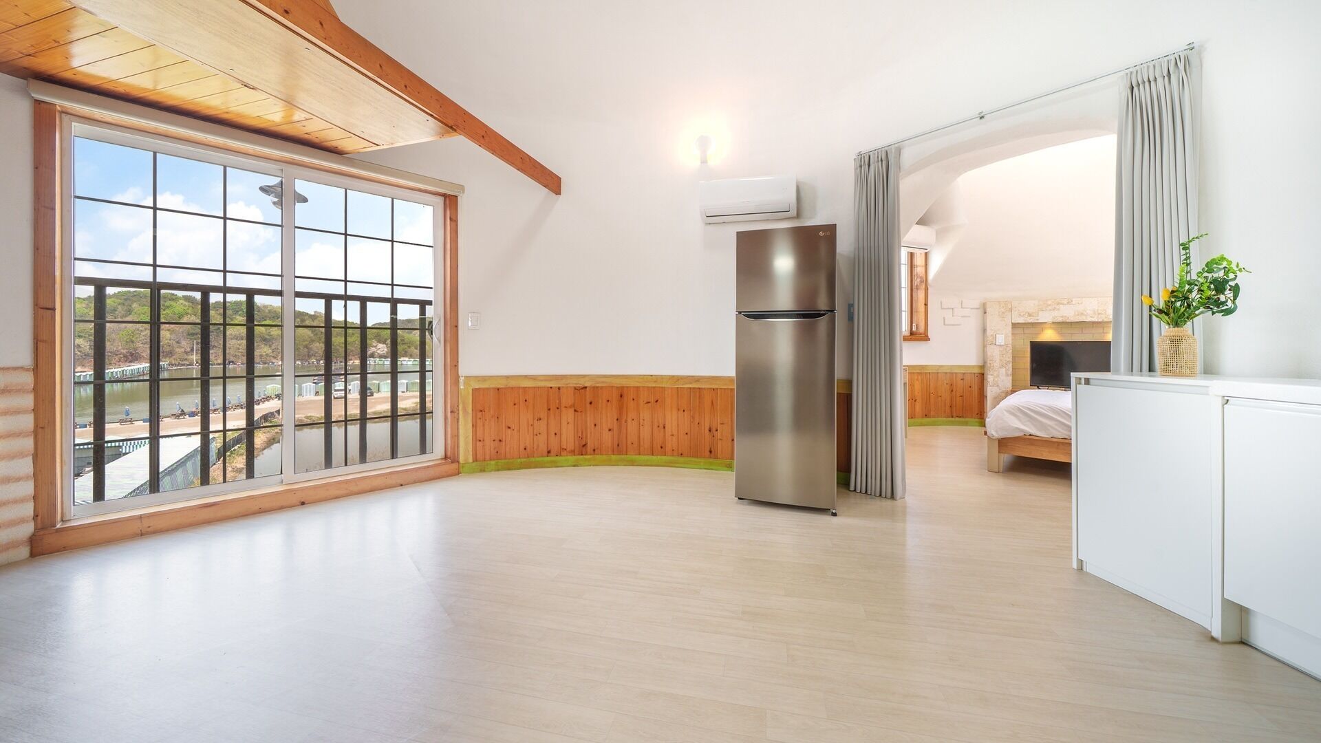 Ein geräumiger Raum mit großem Fenster, einer integrierten Kühlmaschine und einem Bett mit Kopfteil.