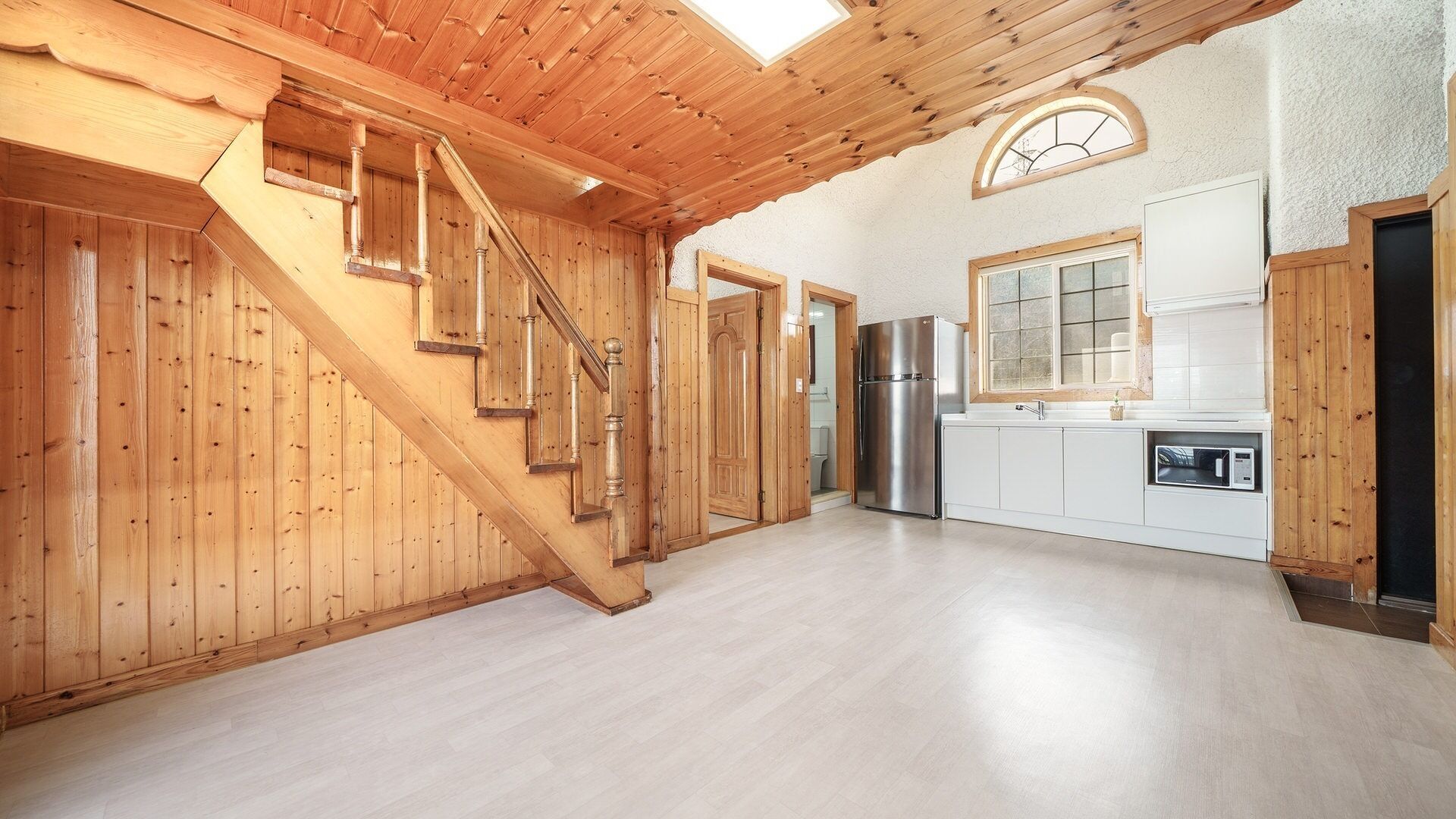 A spacious kitchen with wooden walls and a modern design, featuring a built-in oven and a stainless steel refrigerator.