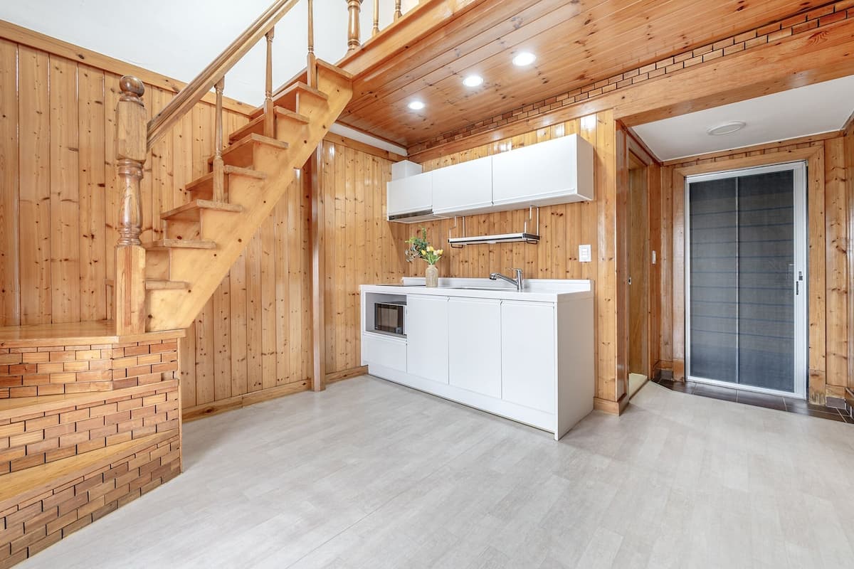 A wooden interior with a kitchen area, a staircase, and a door leading to another room.