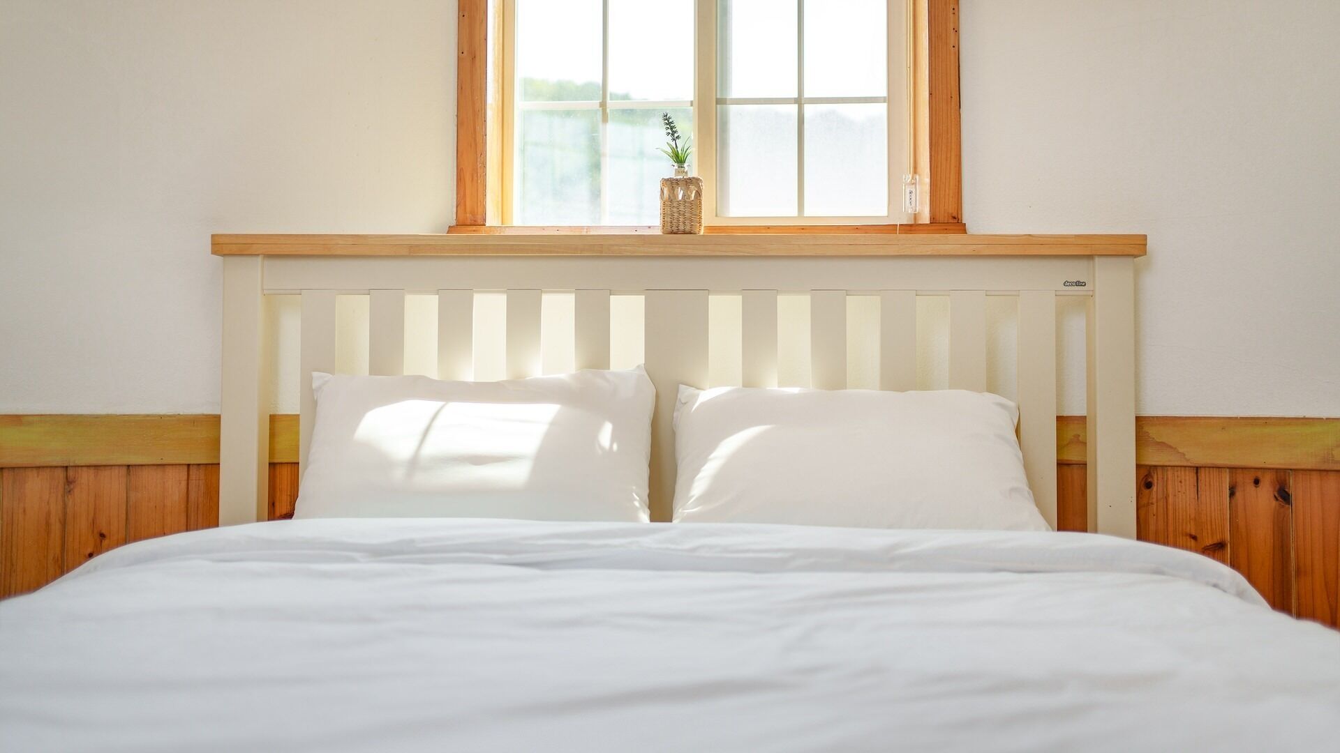 Una cama con ropa de cama blanca, cabecera de madera y una ventana arriba.