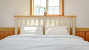 A bed with white bedding, a wooden headboard, and a window above.