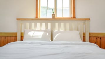Uma cama com roupa de cama branca, cabeceira de madeira e uma janela acima.